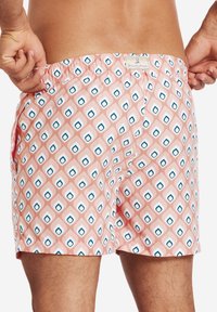 Simshorts i ett rosa geometriskt mönster med vita diamanter och blå konturer. Elastic midja och sidofickor. Slät textur.