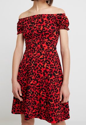 Vrouw die een rode off-shoulder jurk draagt met zwarte en donkerrode luipaardprint en korte pofmouwen.