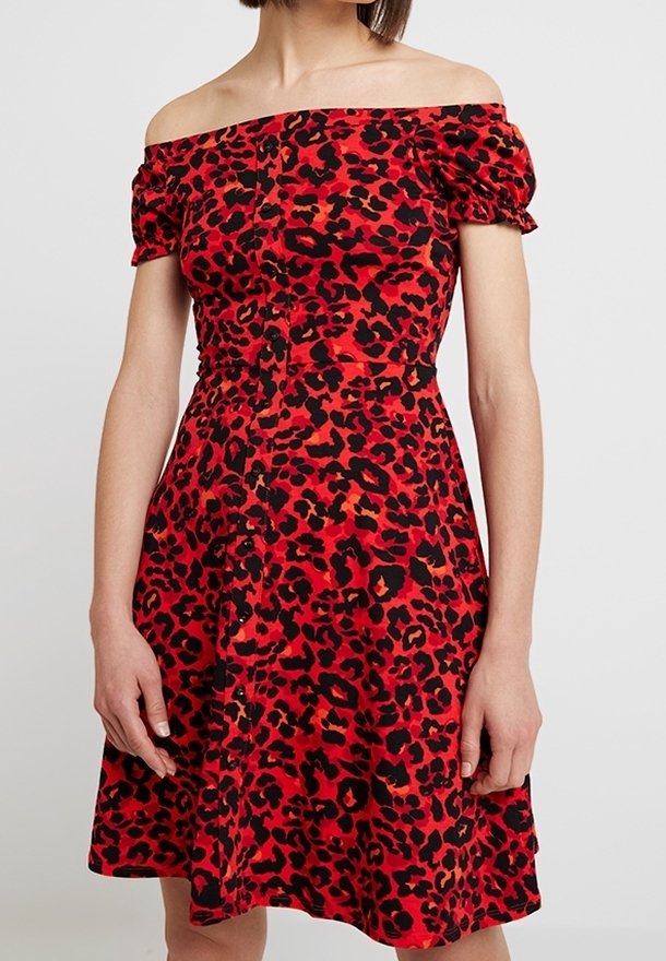 Femme portant une robe rouge épaules dénudées avec un imprimé léopard noir et rouge foncé et des manches courtes bouffantes.