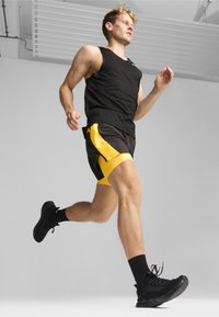 Mustamata varrukateta topp, kollase aktsendiga mustad lühikesed püksid ja mustad spordijalatsid. Sile kangas, sobiv disain ja keskmise reani püksid.