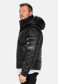 Zwarte leren pufferjack met een capuchon, voorzien van een ritssluiting borstzak en mouwpatches. Glad textuur met een gestikt ontwerp.