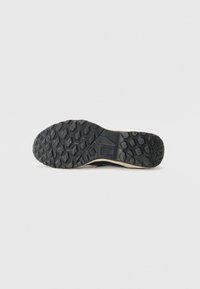 Semelle noire en caoutchouc avec un motif hexagonal texturé, dotée d'un bord beige clair. Construction durable conçue pour la traction et l'adhérence.