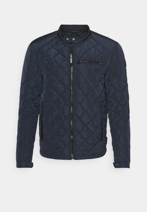 Veste matelassée bleu marine avec col montant, fermeture éclair devant, poches zippées sur la poitrine et les côtés, et fermetures pression aux poignets et au col.