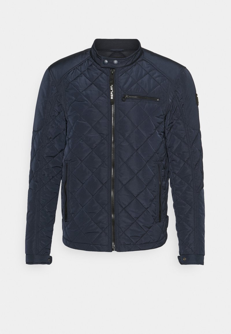 Veste matelassée bleu marine avec col montant, fermeture éclair devant, poches zippées sur la poitrine et les côtés, et fermetures pression aux poignets et au col.