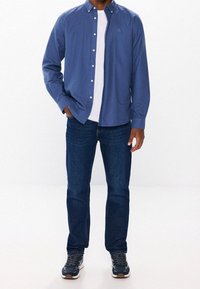 Niebieska koszula na guziki noszona na białym t-shircie, w połączeniu z ciemnoniebieskimi dżinsami i szarymi tenisówkami o teksturowanym wzorze.