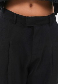 Zwarte taps toelopende broek gemaakt van een gestructureerde stof, met een voorplat, riemlussen en een slanke tailleband met een subtiele glans.