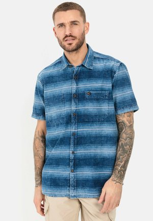 Kortærmet skjorte med knapper i blå denim med vandrette hvide striber, der har en brystlomme og brune knapper. Glat tekstur.
