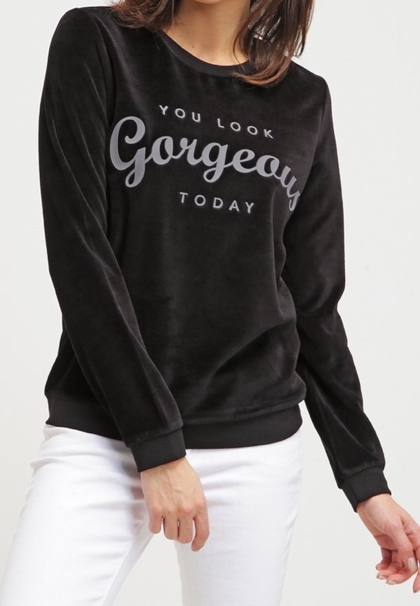 Sudadera de terciopelo negra con mangas largas, puños y dobladillo acanalados. Presenta el texto impreso "TE VES HERMOSA HOY" en gris. Combinada con pantalones blancos.