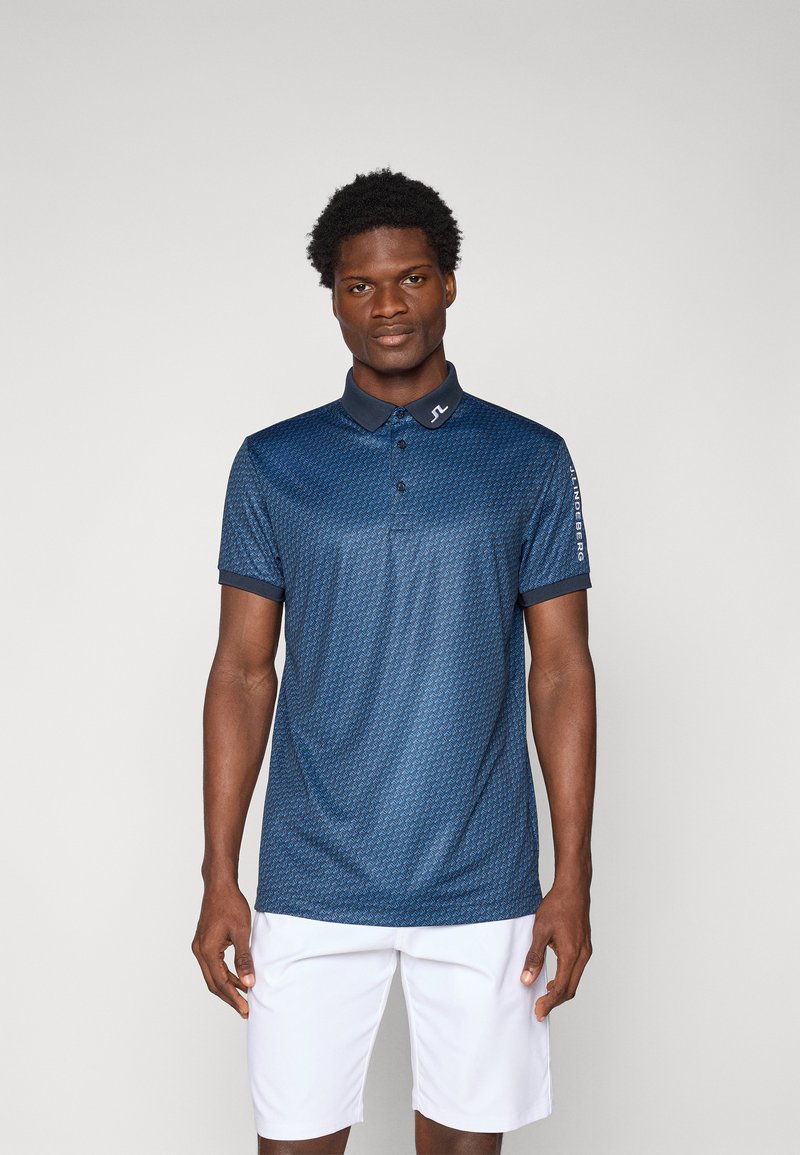 Chemise polo bleu marine avec un motif géométrique, à manches courtes et col. Comprend un logo sur le col et un accent imprimé sur la manche.