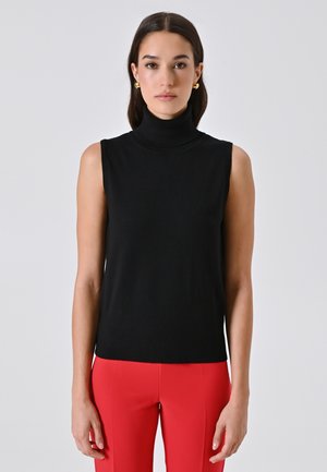 Schwarzes ärmelloses Turtleneck-Top aus Strickstoff mit einer taillierten Silhouette. Getragen mit roten enger geschnittenen Hosen für den Kontrast.