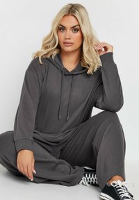 Grå randig hoodie och löst sittande byxor, med dragsko på huvan och sidofickor, tillsammans med svarta canvas sneakers.