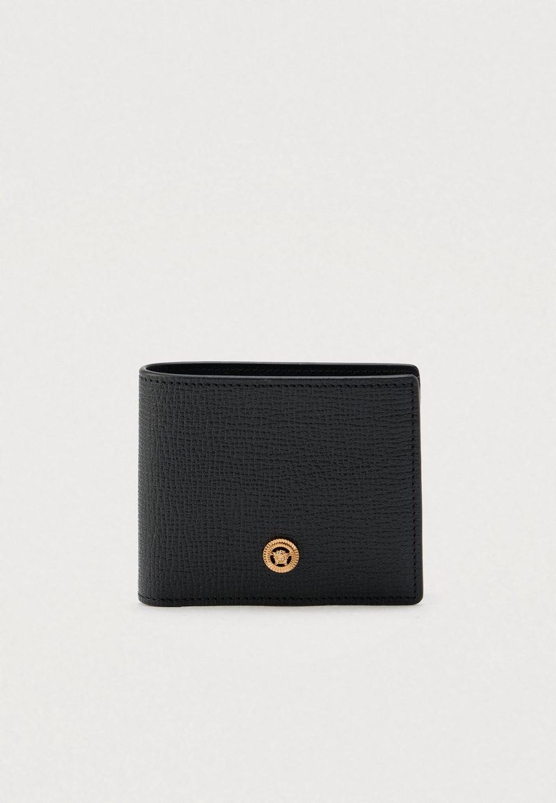 Cartera de cuero negro con textura y un emblema circular dorado. Presenta una forma rectangular compacta con bordes limpios y un diseño minimalista.