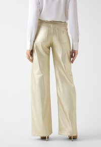 Wijde jeans met broekspijpen in metallic gouden stof, met een gladde textuur, minimalistische stiksels en achterzakken met logo-accenten.