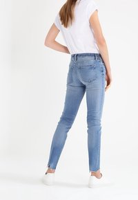Jeans ajustados de color azul claro con un dobladillo ligeramente deshilachado y bolsillos traseros, combinados con una blusa de manga corta blanca y zapatillas blancas.