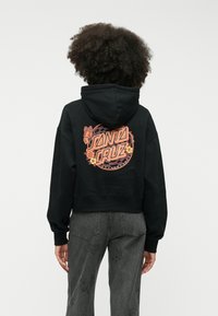 Czarny skrócony hoodie z kolorową grafiką "Santa Cruz" z kwiatami i tło w biało-czarną szachownicę. Miękki materiał i luźny fason.