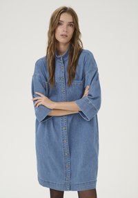 Denim shirt dress in light blue featuring a button-up front, short sleeves, and a relaxed fit with a single chest pocket.