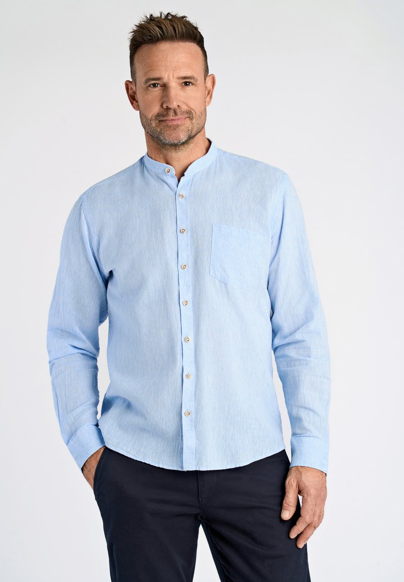 Jasnoniebieska koszula z długim rękawem, z kołnierzykiem mandaryńskim, kieszenią z przodu i zapięciem na guziki. Materiał ma subtelną teksturę i połysk.