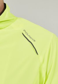 Veste jaune vif en tissu léger, dotée d'un grand col, d'un logo imprimé "ENDURANCE" et d'accents noirs sur les épaules.