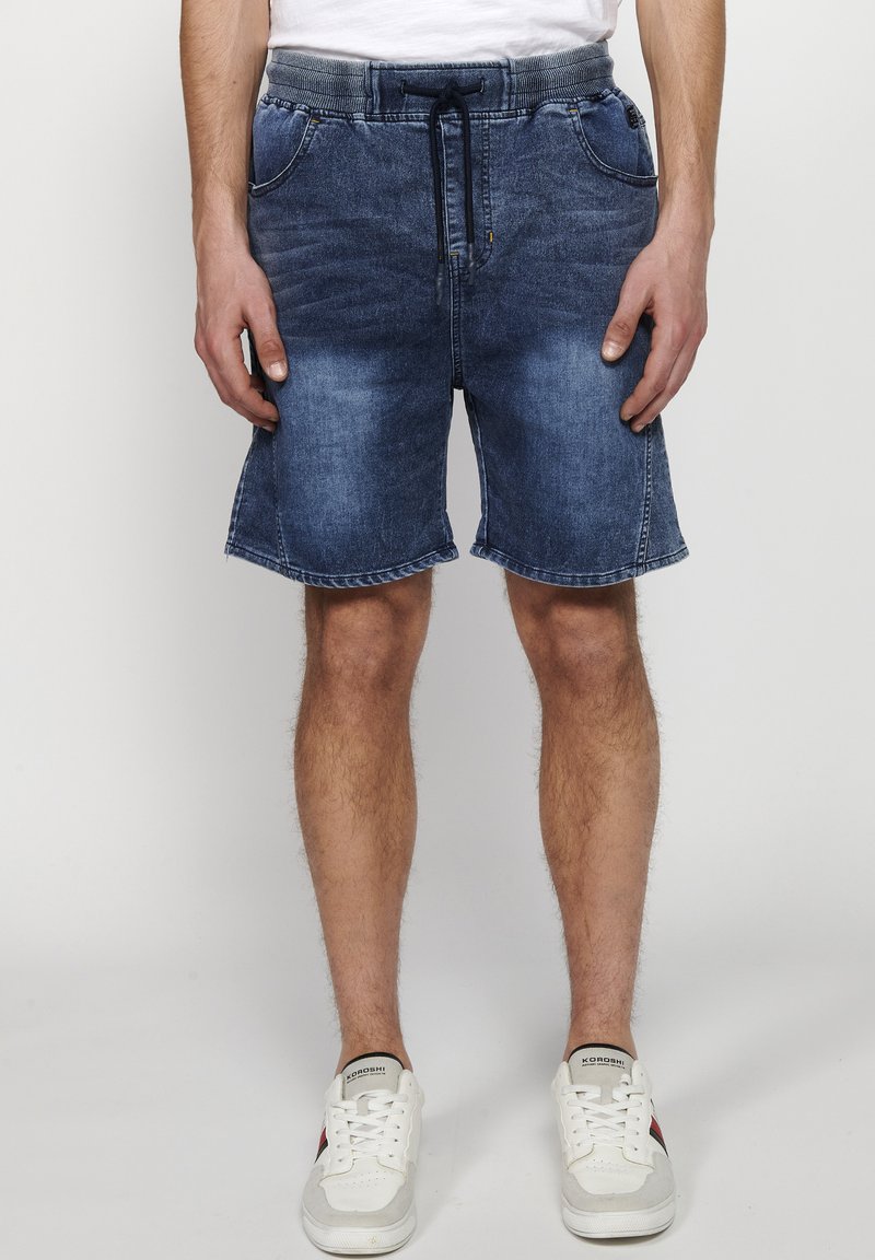 Jeansshorts i medelblå färg med dragsko i midjan, fem fickor och rak passform. Har lätt blekning och en rå fåll.