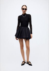 Black dress featuring a textured lace bodice and a voluminous satin skirt. Paired with black flats and minimalist sunglasses.