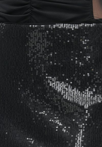 Primeiro plano de um tecido preto com densas fileiras verticais de pequenas lantejoulas brilhantes refletindo a luz.