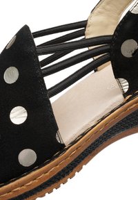 Černá sandála s stříbrnými puntíky, elastickými pásky, béžovou stélkou označenou velikostí 37 a strukturovanou hnědo-černou podrážkou.