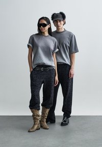 Gray graphic t-shirts, loose black patterned pants, and patterned boots. Accessories include sunglasses and a fur-accented cap.