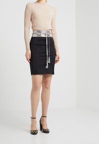 Haut beige à manches longues côtelé, jupe noire cintrée avec une ceinture à imprimé serpent. Talons noirs avec des pois dorés, textures de tissu lisses et formes définies.