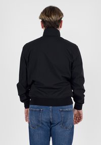 Giacca bomber nera con colletto alto, caratterizzata da una superficie esterna liscia e polsini elastici, abbinata a jeans in denim blu.