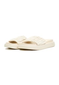 Paire de sandales crème à enfiler avec des brides épaisses matelassées et des semelles en caoutchouc plates, présentées sur fond blanc.