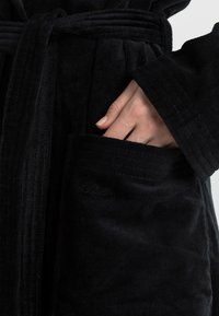 Black robe made of soft, textured fabric with a belted design. Features a side pocket with embossed branding.