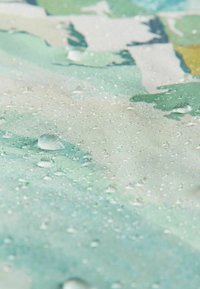 Des gouttes d'eau perlant sur une surface de tissu imperméable à motifs verts et blancs.