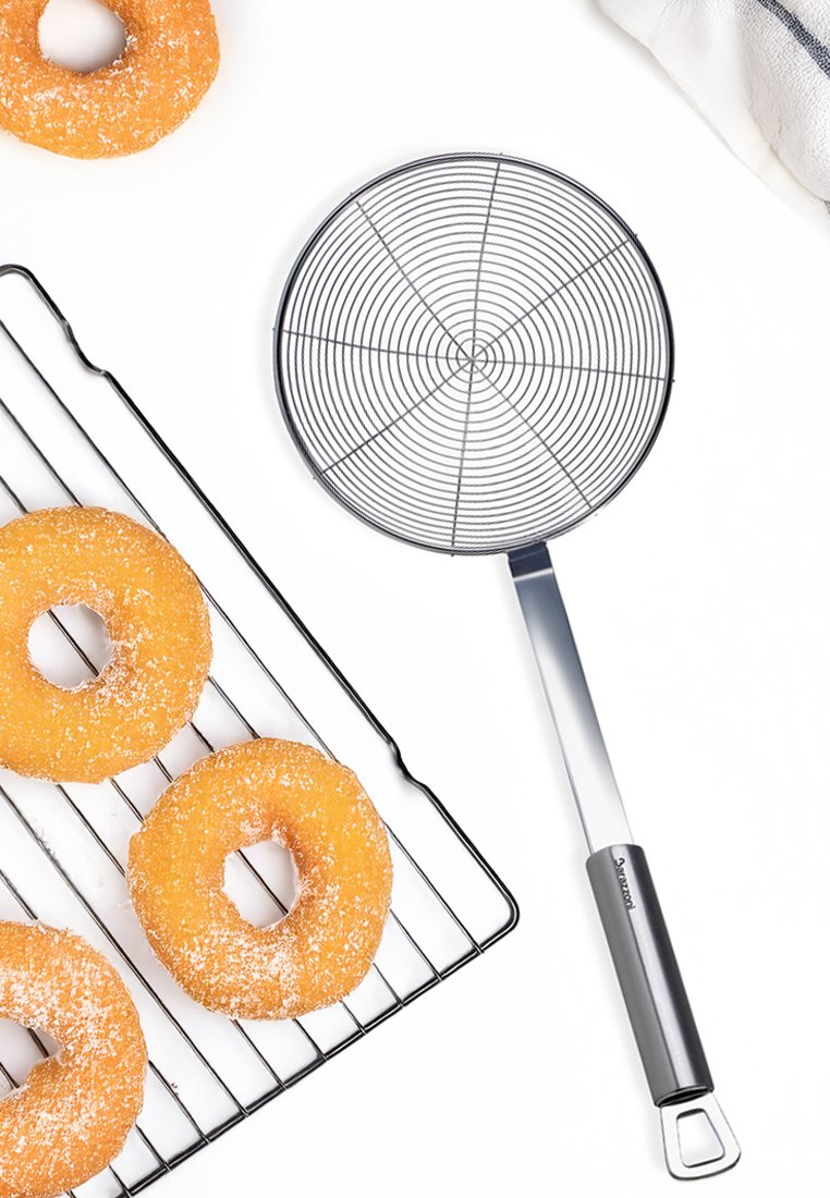 Skimmer de alambre con malla circular y mango de acero inoxidable, al lado de cuatro donuts dorados sobre una rejilla de enfriamiento negra.