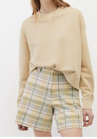 Sudadera beige con hombros caídos combinada con pantalones cortos de cuadros amarillos claros que presentan detalles en verde y azul, con cierre de botón visible.