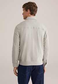 Helehall mantel kraega, tekstureeritud kangast ja pikkade varrukatega. Sellel on äärega alumine serv ja nööpidega mansetid. Kandmist tumeda teksaga.