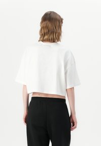 Tricou alb scurt, cu mâneci scurte, croială lejeră și decolteu rotund. Purtați cu pantaloni negri cu talie înaltă. Design simplu, fără modele vizibile.