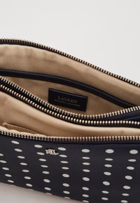 Navyfärgad plånbok med polkador, guldens detaljer, två dragkedjefickor och beige inredning. Har en varumärkesetikett inuti.