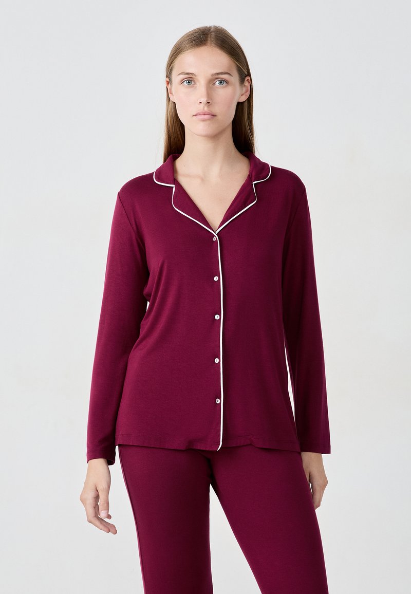 Ensemble de pyjama en coton bordeaux comprenant des manches longues, un col à revers avec passepoil blanc et une fermeture à boutons sur le devant. Texture lisse et coupe ajustée.