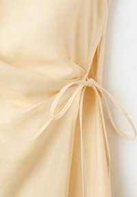 Material bej deschis adunat și legat într-o fundă ordonată pe lateral, arătând o textură netedă și pliuri ușoare.