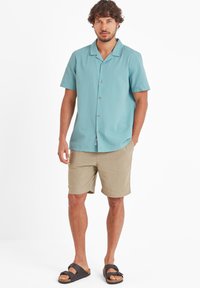 Short-sleeve, light blue textured shirt with a collar, buttons down front, paired with tan shorts and dark sandals.