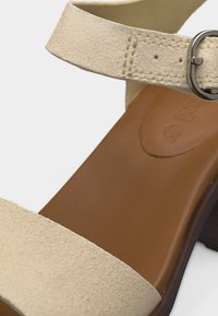 Πέδιλο με λουράκι στον αστράγαλο από μπεζ καστόρι, ασημένια αγκράφα, καφέ δερμάτινη σόλα και τακούνι τύπου block.