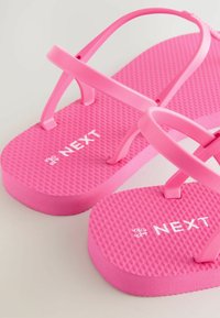 Vaaleanpunaiset flip-flopit, joissa on teksturoidut pohjat ja hihnat. Sileä, kestävä materiaali, jossa on valkoinen "NEXT"-logo. Kevyt ja rento muotoilu.
