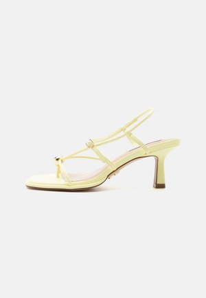 Yellow strappy high-heeled sandal with an adjustable buckle and a mid-height slim heel on a white background.