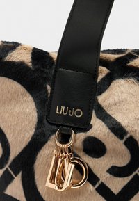 Primo piano di una borsa con texture in pelliccia, con un motivo nero e beige, tracolla in pelle nera con "LIU·JO" in oro e charm a lettere in tonalità oro appesi.