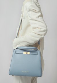 Strukturirana torba svijetloplave teksturirane kože sa zlatnim hardverom, s gornjom ručkom i podesivim remenom za nošenje preko tijela.