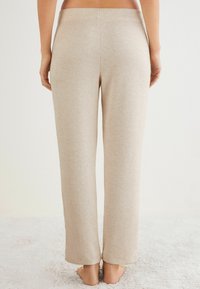 Beige loungebroeken van een zachte, textuurstof; wijde pijpen; elastische tailleband; naadloze achterkant en geen zichtbare zakken of hardware.