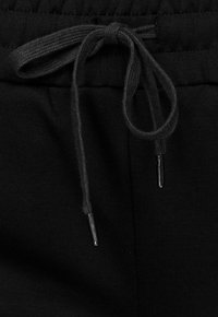 Črne športne hlače so izdelane iz teksturiranega blaga, imajo elastičen pas in zategovanje s črpalko z metalnimi zaključki.