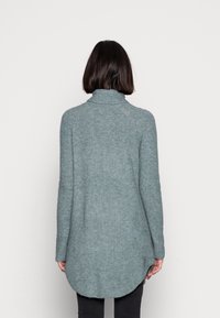 Světle modrý svetr s dlouhým rukávem a rolákem, s texturovaným úpletem, žebrovanými detaily, zakřiveným lemem a spadlými rameny, pohled zezadu.