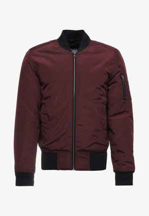 Burgundijas bomber jakas ar rāvējslēdzēja aizdari, ribotām aprocēm un apakšmalu, kā arī rāvējslēdzēja kabatu uz piedurknes. Gluda, spīdīga auduma ar polsterētu izskatu.