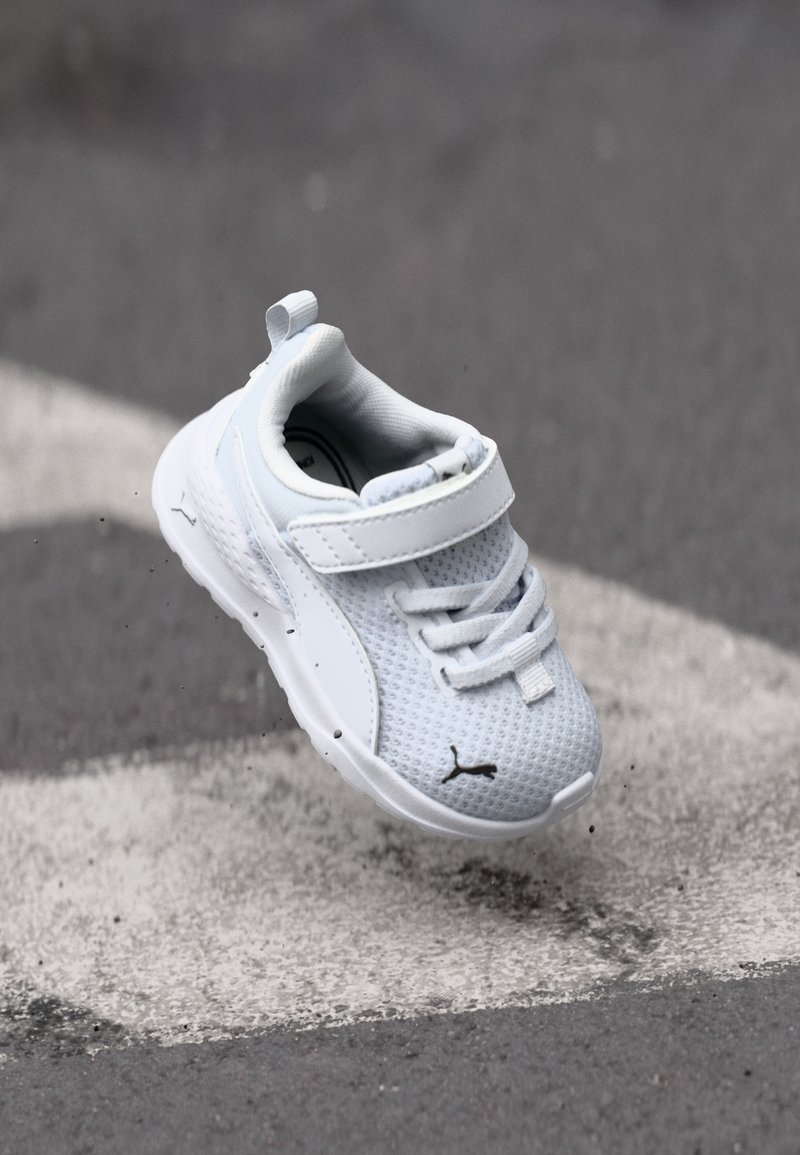 Weißer Sneaker mit Mesh-Obermaterial, gepolstertem Kragen und elastischen Schnürsenkeln. Verfügt über einen Klettverschluss und ein schwarzes Logo an der Seite. Leichtes Design.